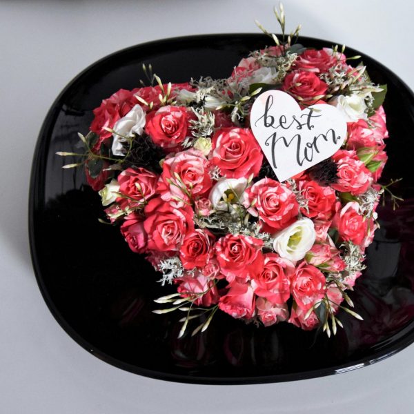 Muttertag Der Blütenwald Floral Design rosarot-farbenes Gesteck Herz geschmückt auf schwarzem Teller